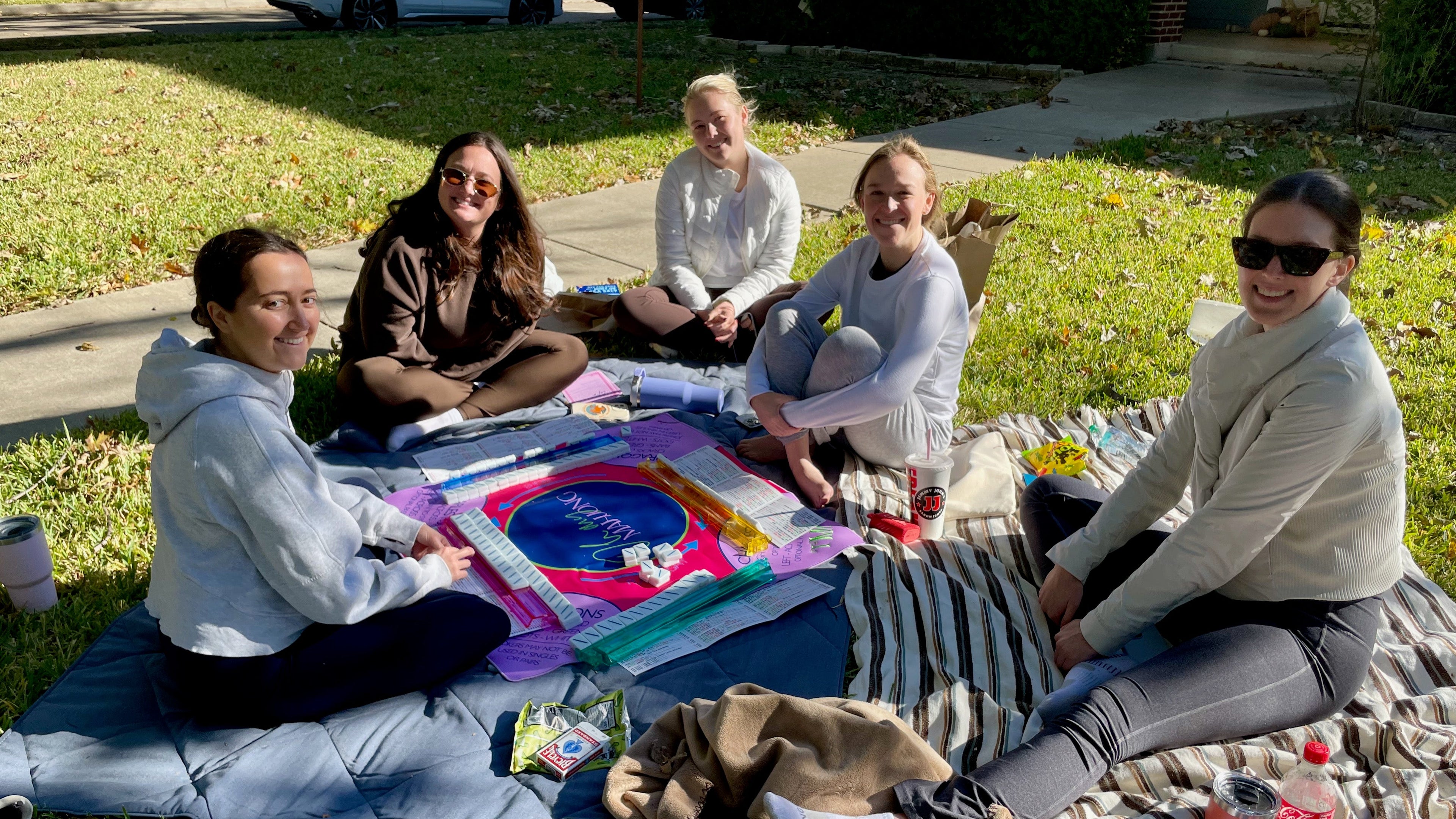 Five neighborhood women playing mahjong outside on the front lawn grass.